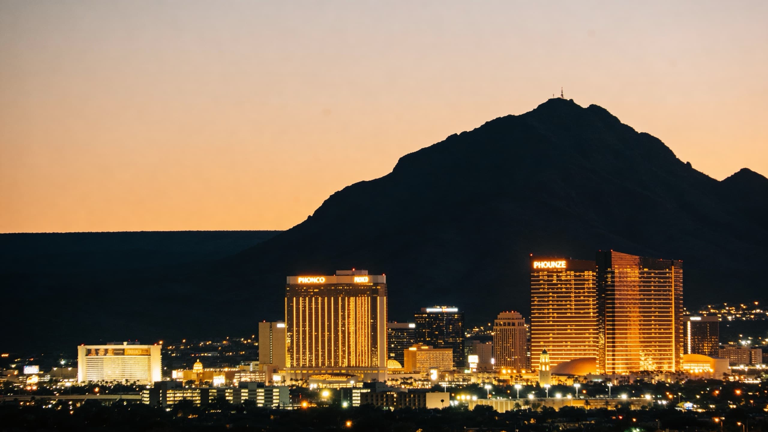 The Phoenix skyline at night, warm gold city lights and Camelback Mountain against a deep black sky